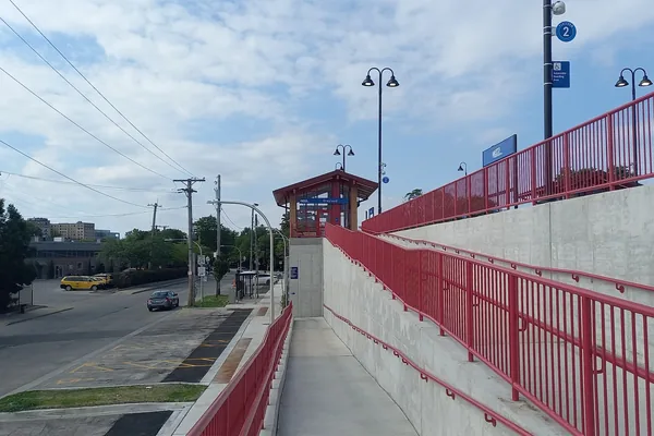 Long concrete access ramp with red handrails rising to a station platform