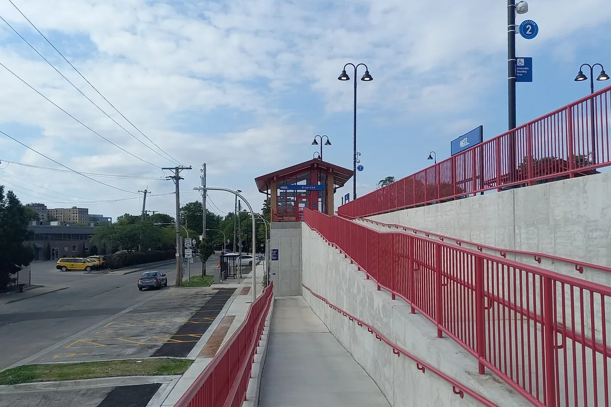 Long concrete access ramp with red handrails rising to a station platform