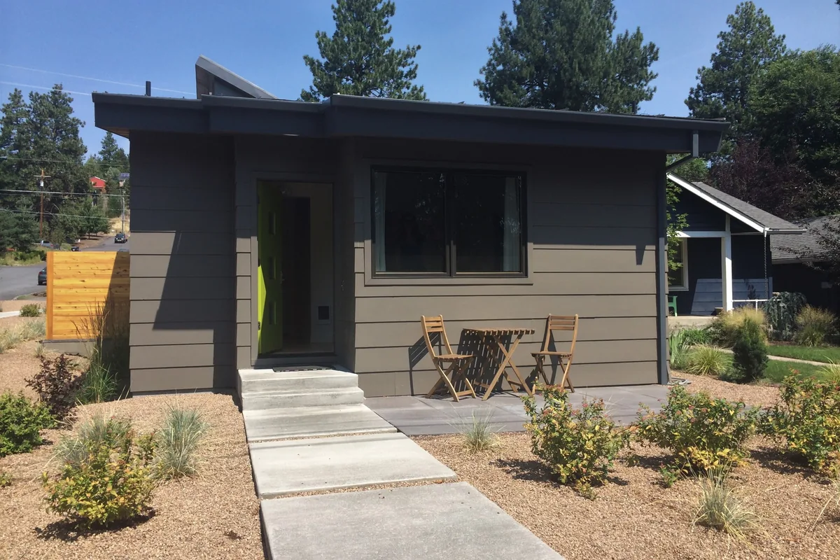 Small detached backyard cottage with a concrete walk and patio in a dry garden