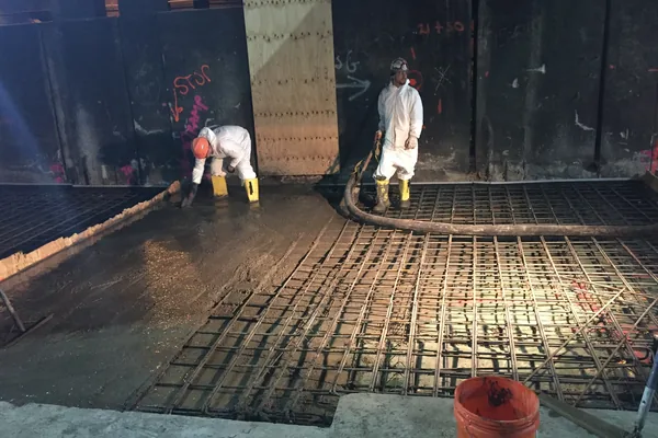 Workers placing a concrete floor slab over a rebar mat from a pump hose