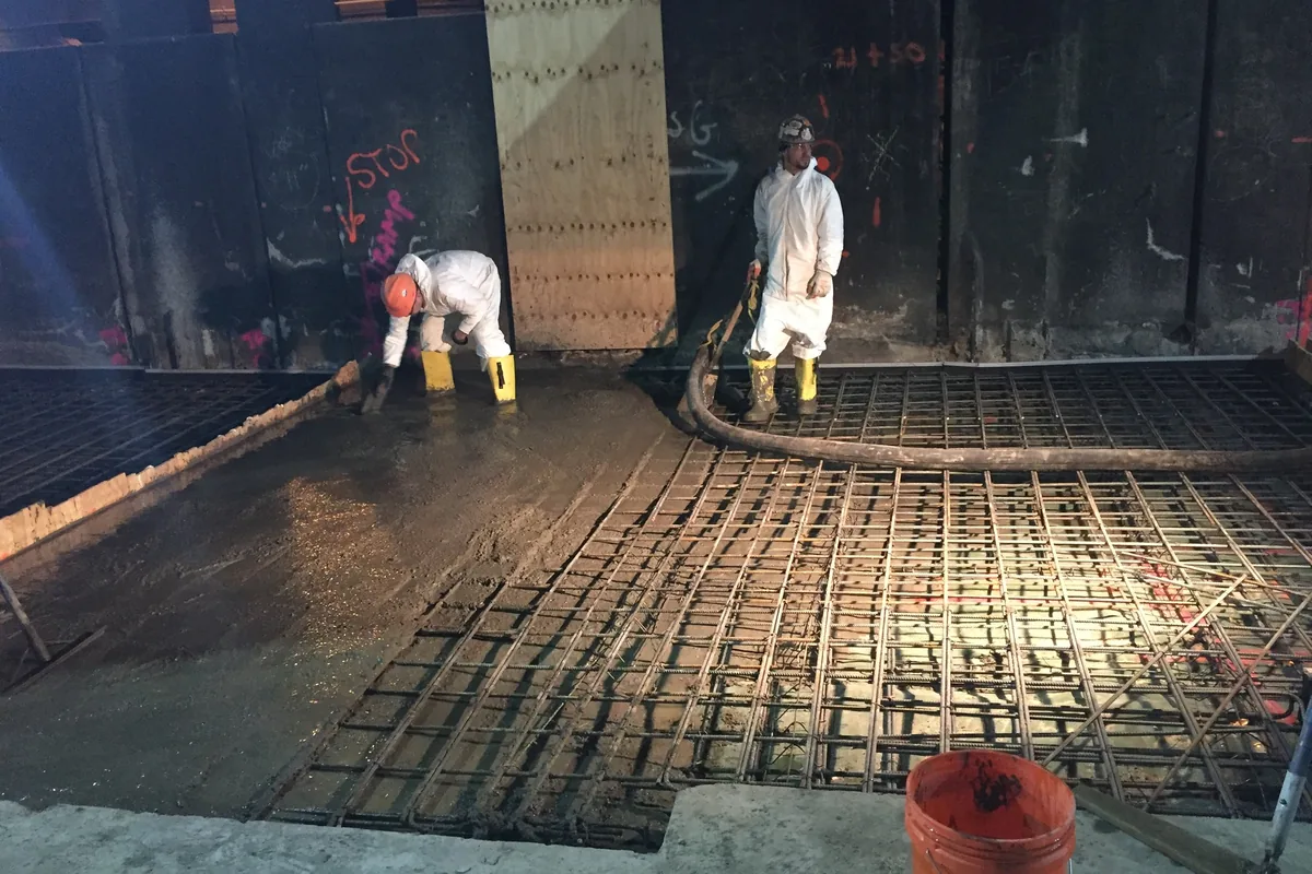 Workers placing a concrete floor slab over a rebar mat from a pump hose
