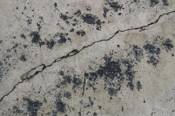 Weathered concrete surface with a crack running across it and dark stains