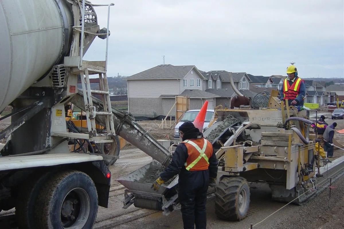 Mixer truck feeding a slipform machine that extrudes a new concrete curb