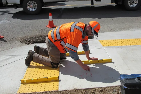 Inspector measuring a new concrete curb ramp with yellow truncated-dome warning panels