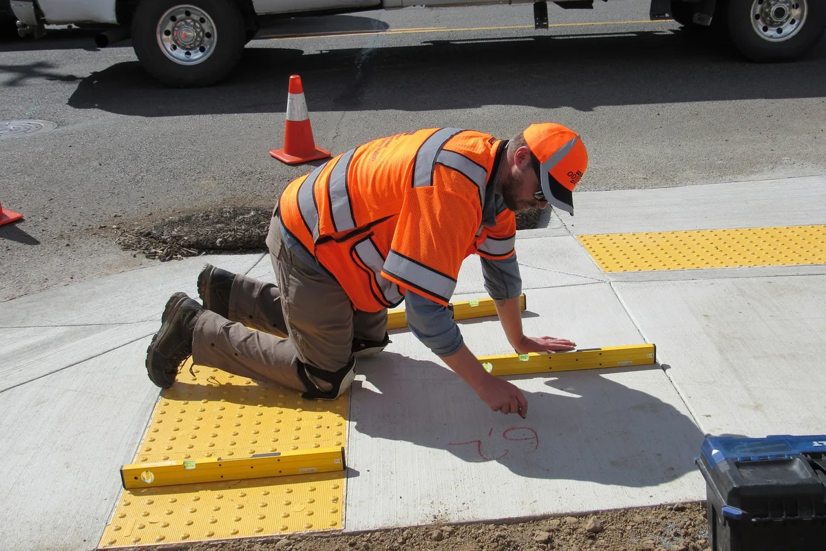 Inspector measuring a new concrete curb ramp with yellow truncated-dome warning panels