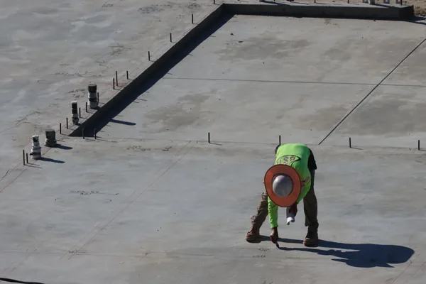 Worker marking layout lines on a new slab foundation with anchor bolts and plumbing stubs