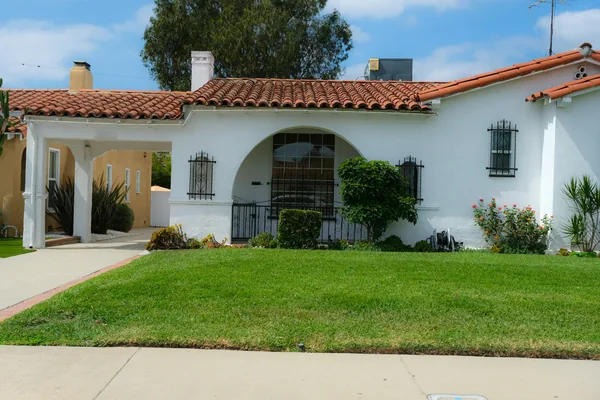 White Spanish-style house with a red tile roof and a concrete walk crossing the lawn to the door