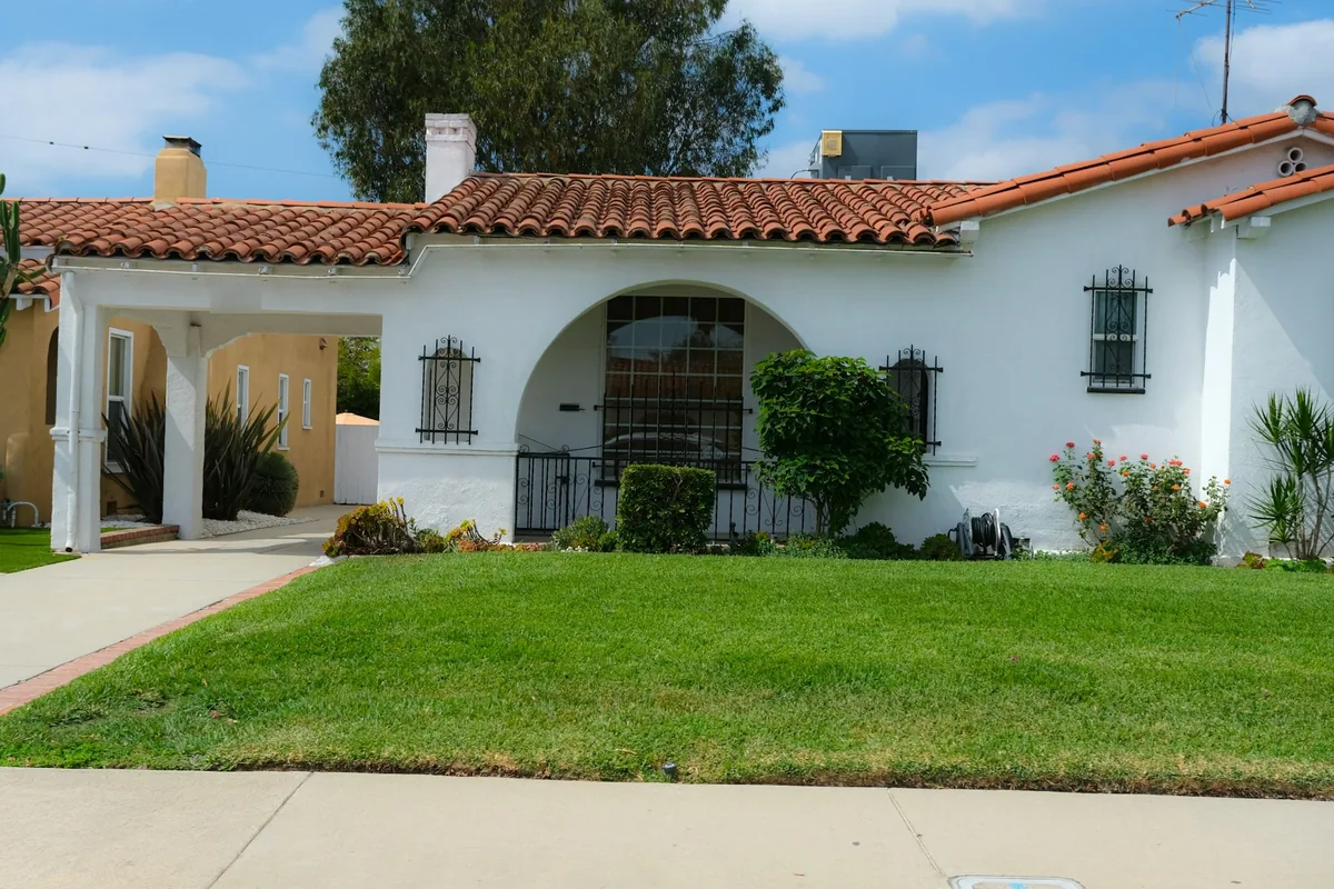White Spanish-style house with a red tile roof, an arched entry and a front lawn, with a driveway along its left side