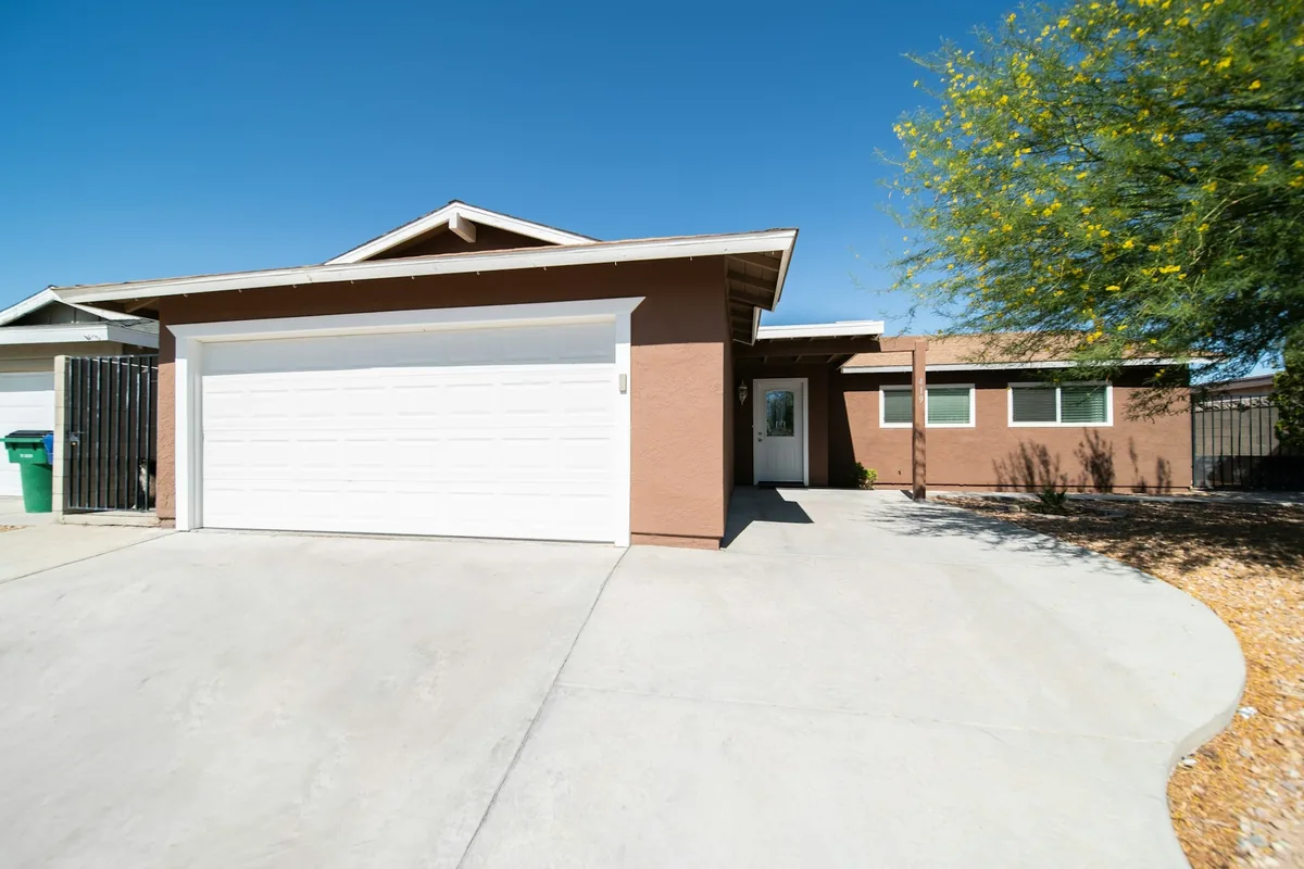 Single-story stucco house with a white two-car garage door and a wide new concrete driveway