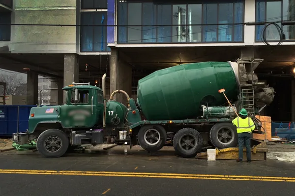 Ready-mix concrete truck parked at a building site while a worker stands at its chute