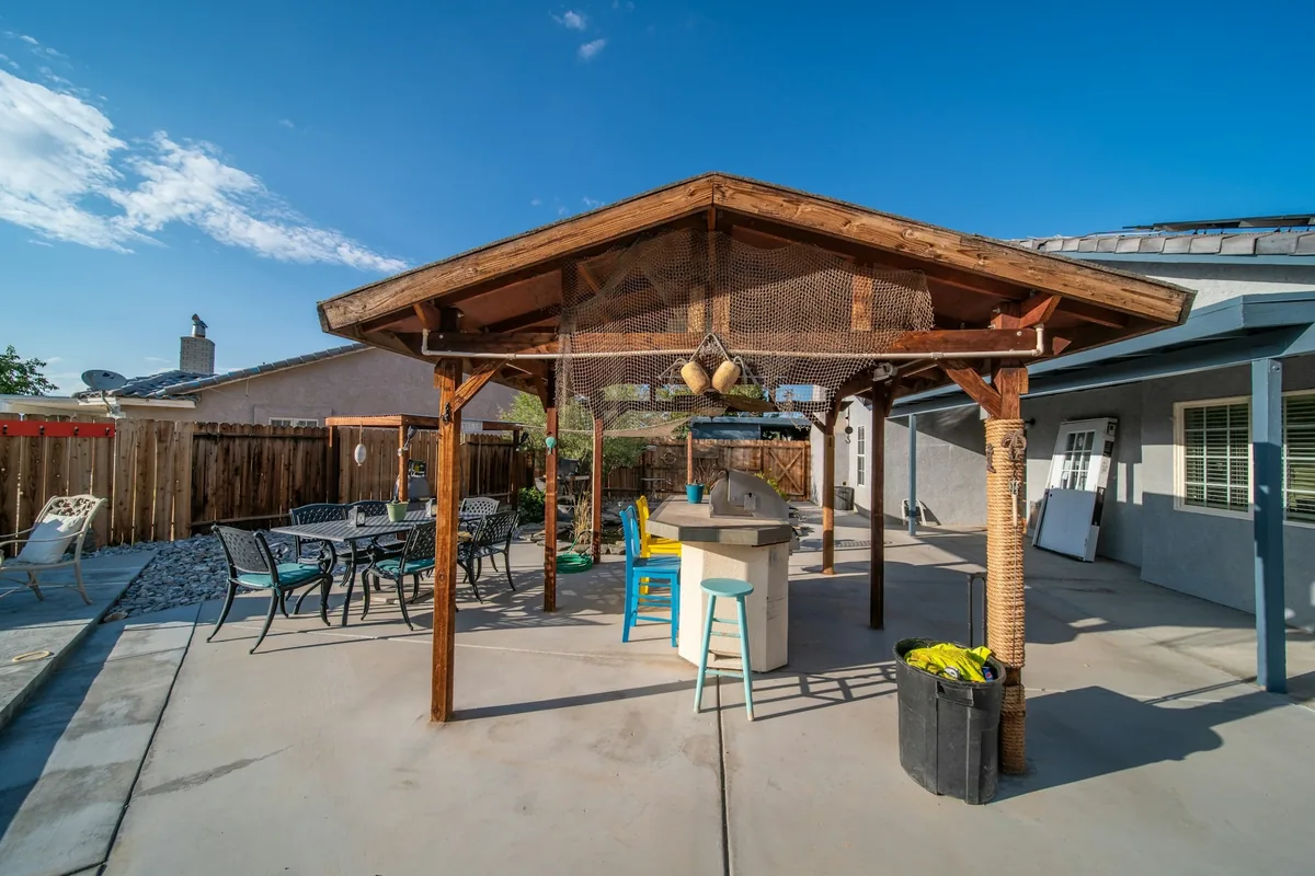 Concrete patio under a wood patio cover with a dining set, beside a wood fence