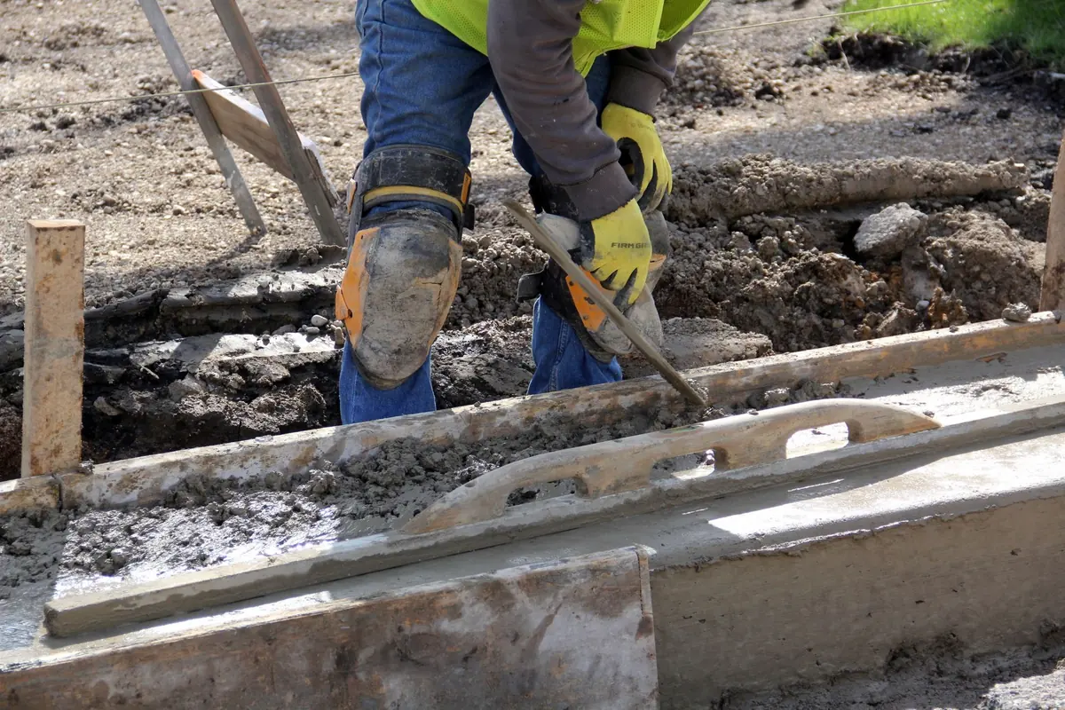 Worker smoothing fresh concrete between wood forms with a float