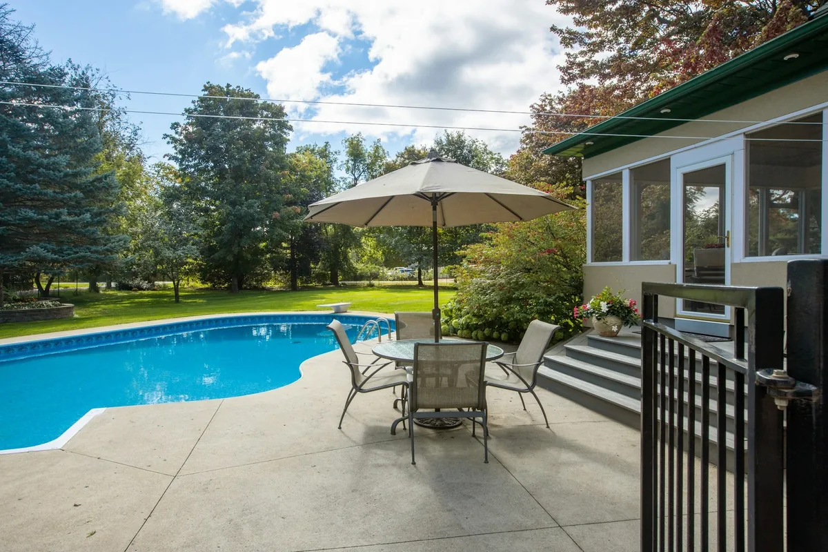 Broom-finished concrete deck around a curved backyard pool with a patio table and umbrella
