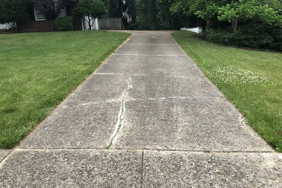 Old concrete driveway with a long crack running down its panels between two lawns